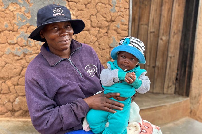 HALO deminer, Precious, holds her baby Tatenda on her lap whilst wearing HALO uniform