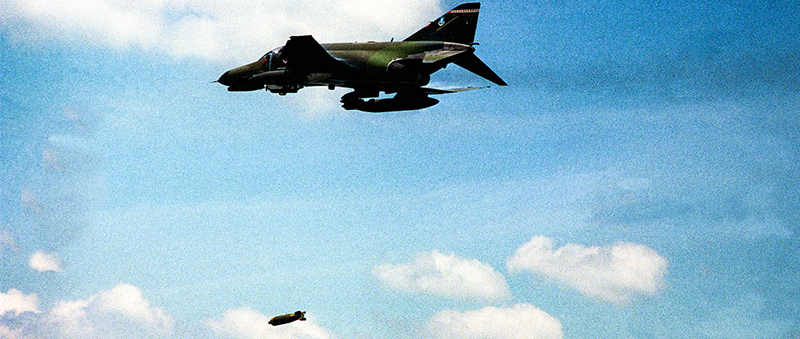 An F4 Phantom dropping a cluster munition canister from the sky 